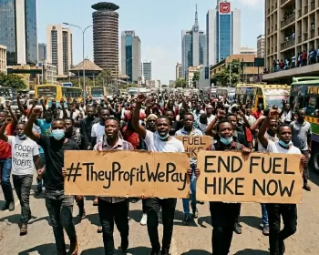 Protesters in Nairobi holding up placards protesting the Iran war. The placards say We Pay They Profit